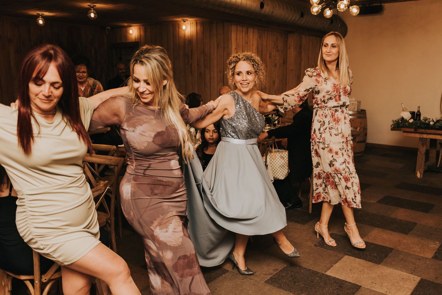 Wedding guests dancing and celebrating on a dance floor at an indoor reception venue with warm lighting.