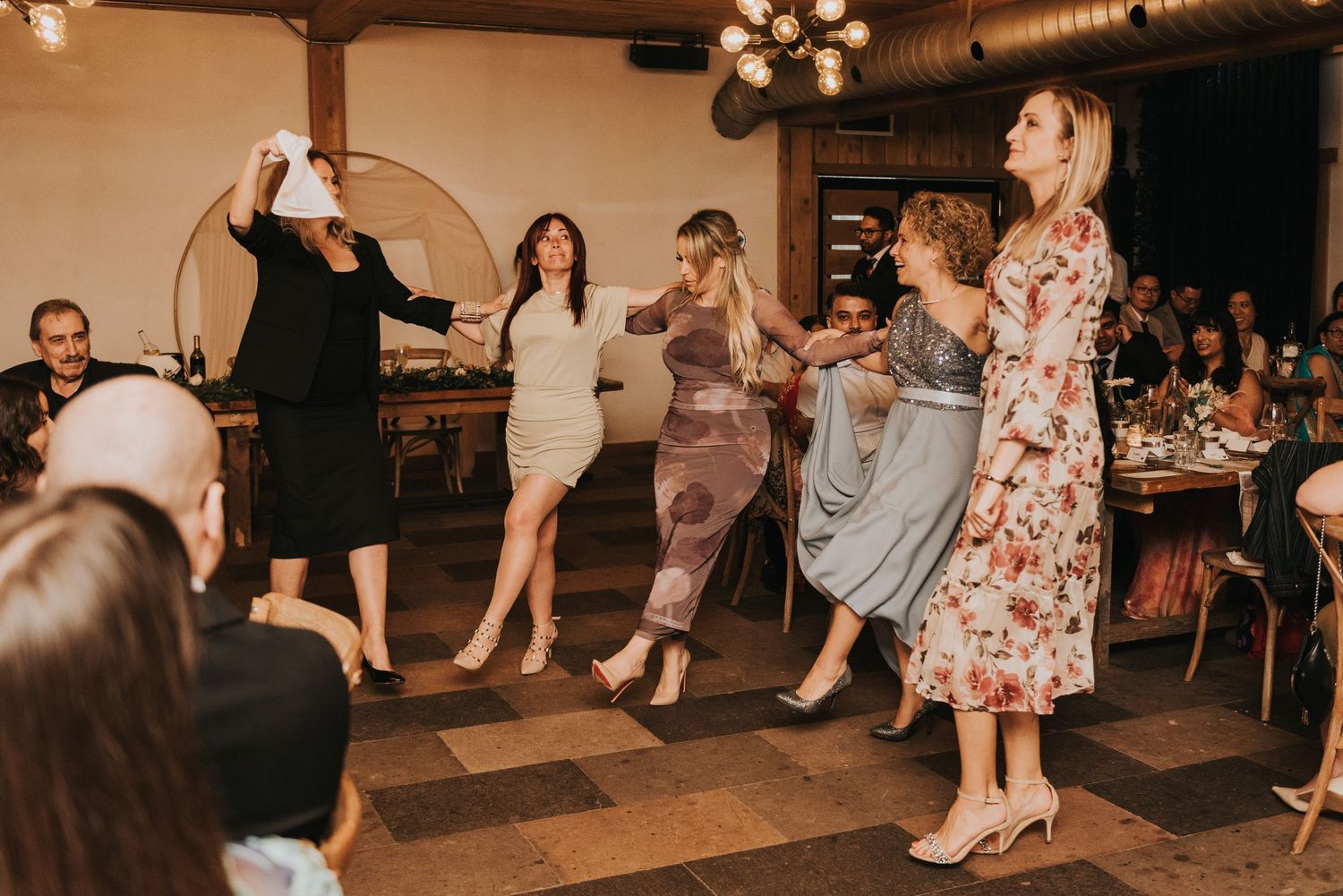 Party guests enjoying themselves on a dance floor with string lights overhead in a rustic venue.