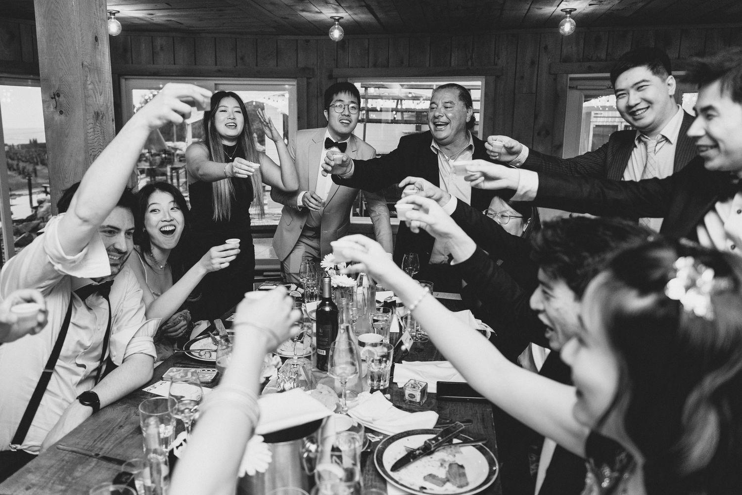 Wedding guests raise their glasses in celebration at a dimly lit reception venue.
