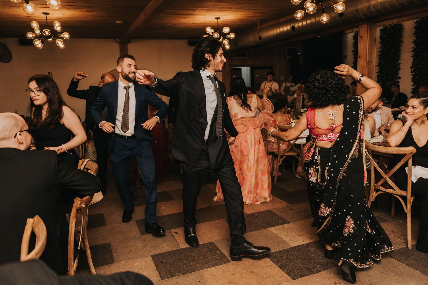 Wedding celebration showing multiple guests dancing and socializing in a warmly lit indoor space.