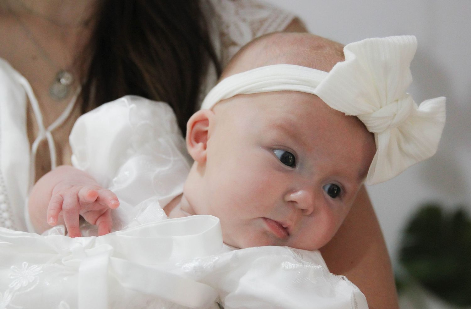 A little girl dressed in a white christening gown with a white bow at her christening