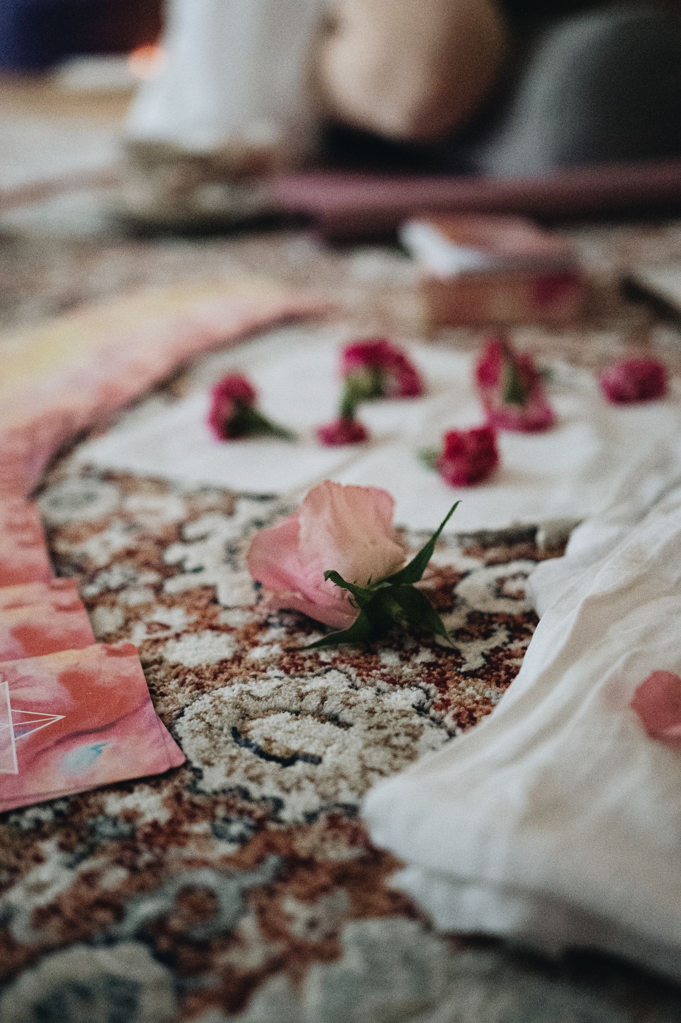 Pink and red rose petals scattered on a textured surface with fabric and papers creating a romantic still life composition.
