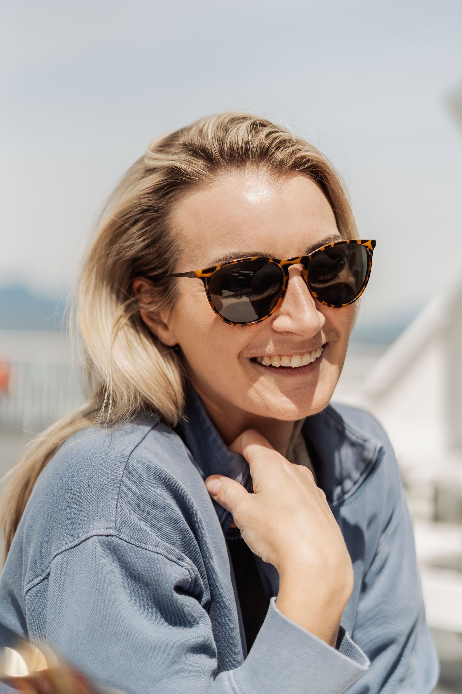 woman in a blue sweat shirt and sunglasses smiles  on a boat during dating photography shoot