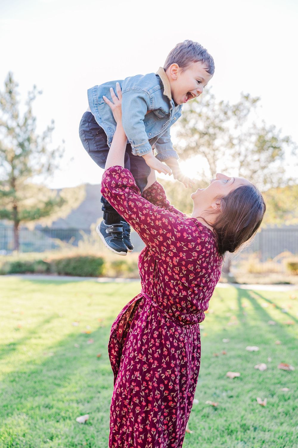 Parent and child play together in a grassy field at sunset, lifting and twirling with joy.