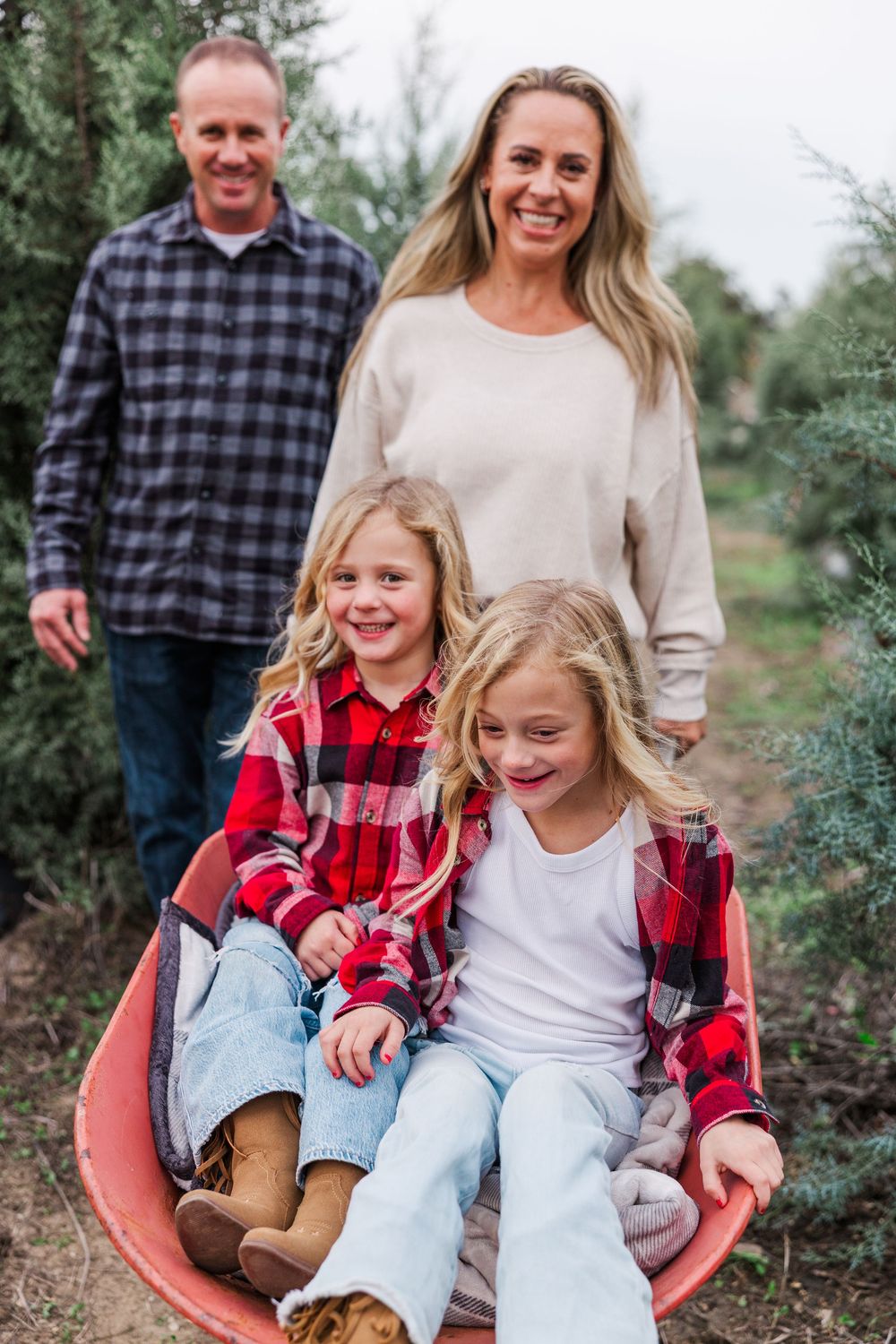 A family enjoying a fun moment together sitting in a red wheelbarrow in a garden setting.