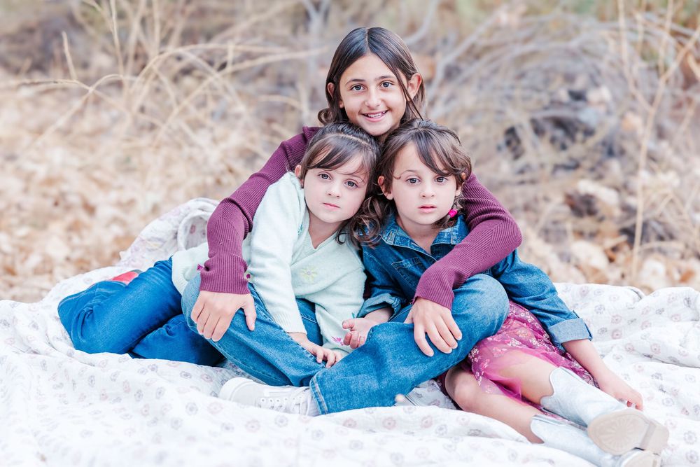 Family members sitting together on a white fence in a snowy winter setting during a photo session.