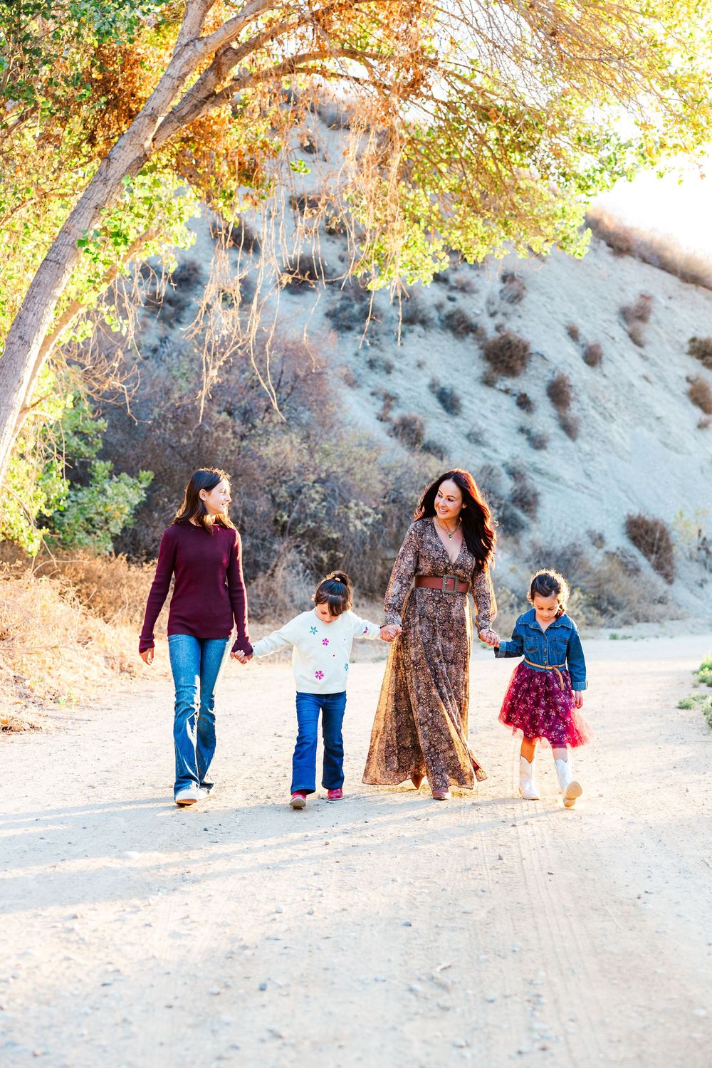 A family walking together on a dirt path under golden autumn trees in a park setting.