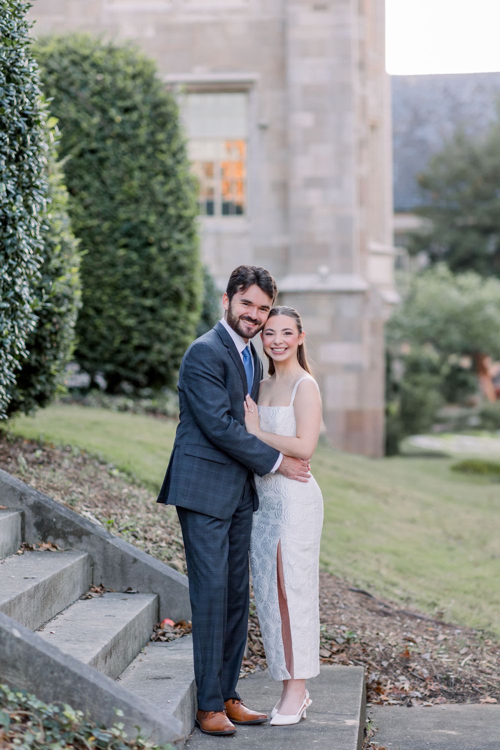 Romantic couple poses on stone steps outside historic building during engagement photoshoot.