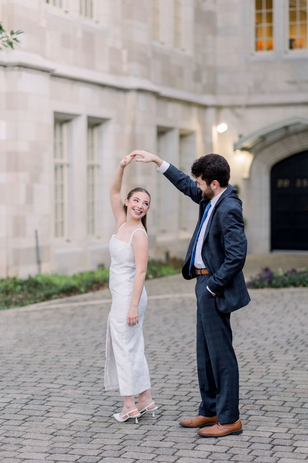 Playful couple dances together on cobblestone courtyard near stone building.