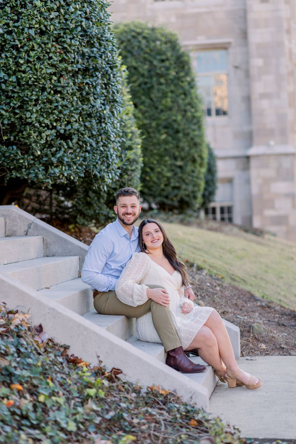 Couple relaxes on concrete steps surrounded by greenery during photo session.
