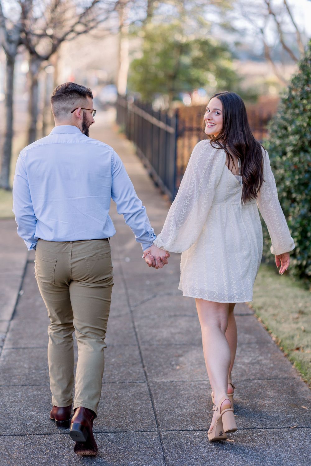 Couple walks hand in hand along outdoor path during engagement shoot.