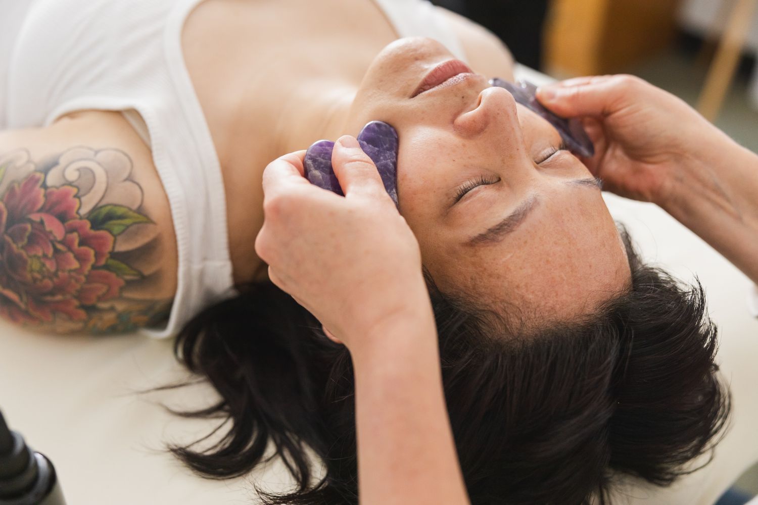 woman laying on table eyes closed amethyst gua sha stones on face for service treatment acupuncture clinic Maple Valley, WA