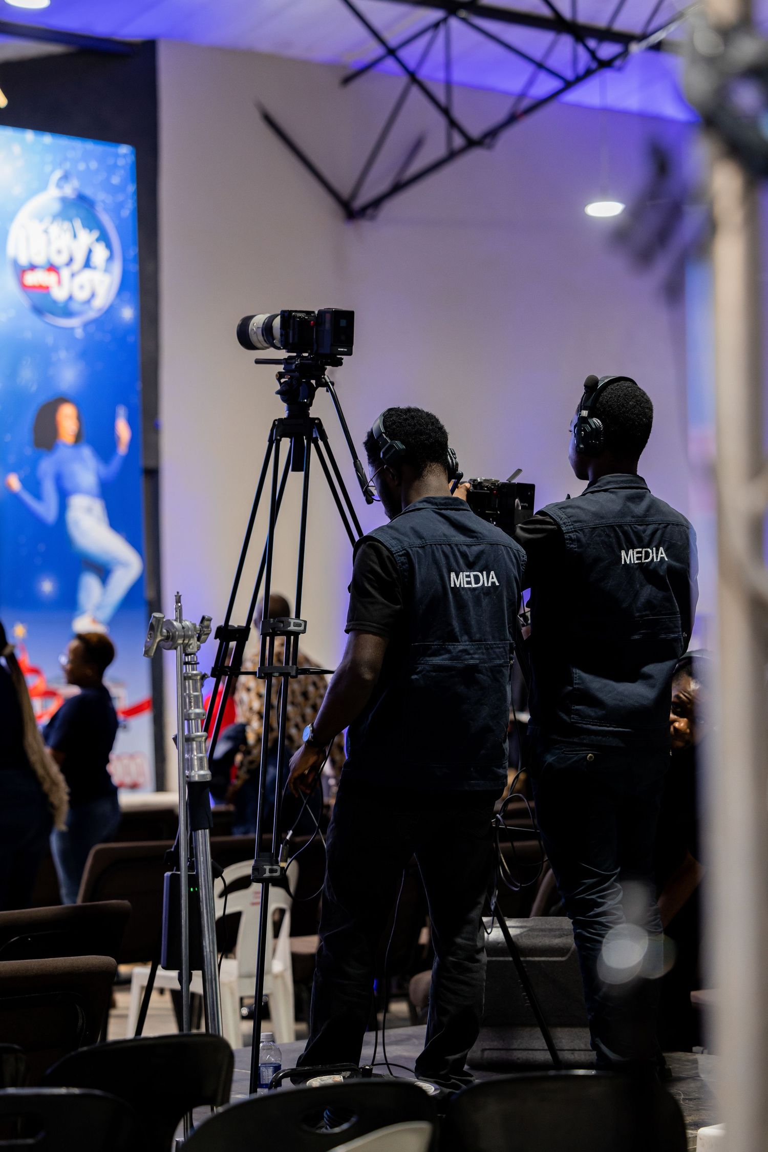 Silhouettes of media crew and camera equipment set up against blue-lit backdrop during event coverage.