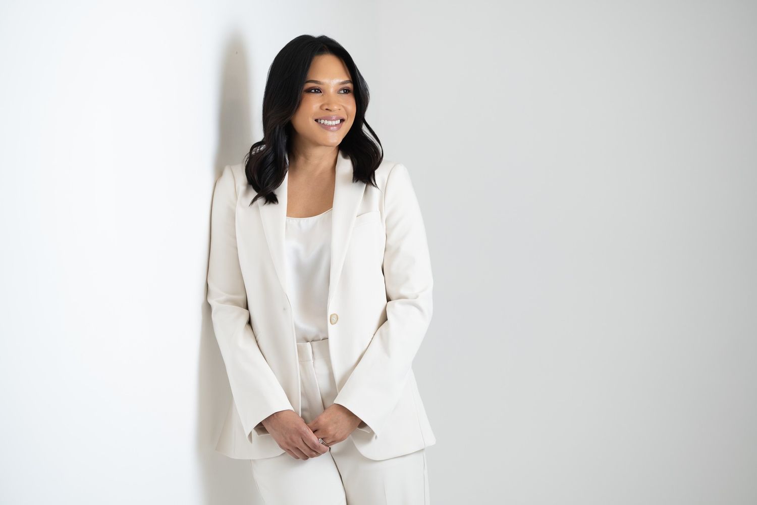 Professional in white blazer and top smiling against light background in business headshot series.