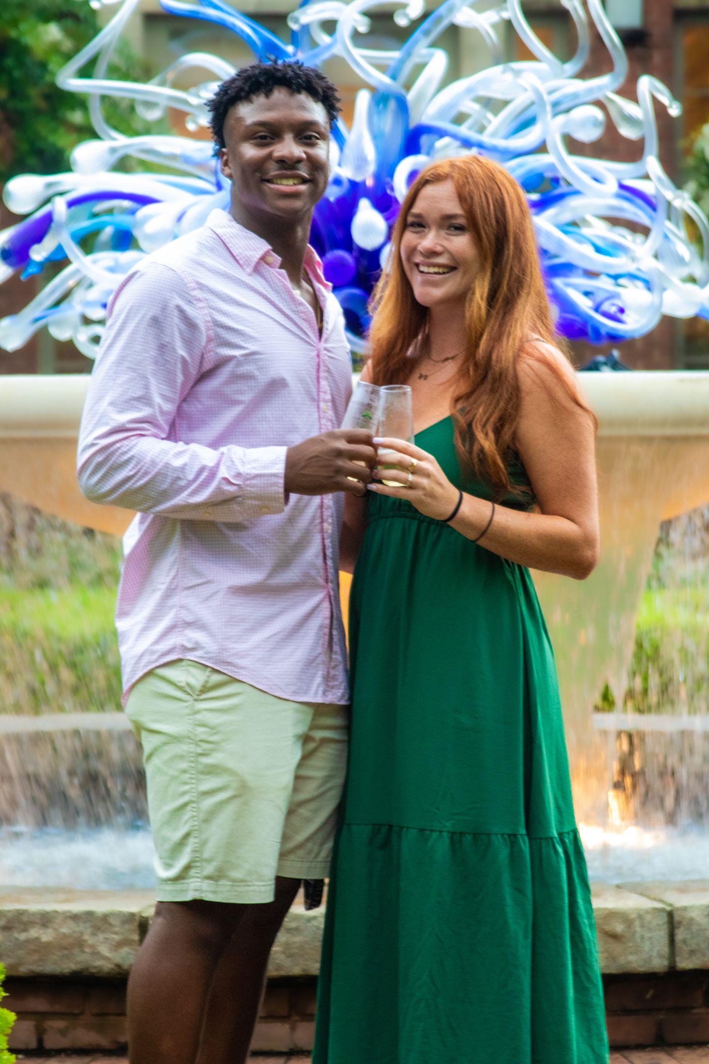 A couple embraces romantically near a garden fountain with yellow flowers and greenery in the background.