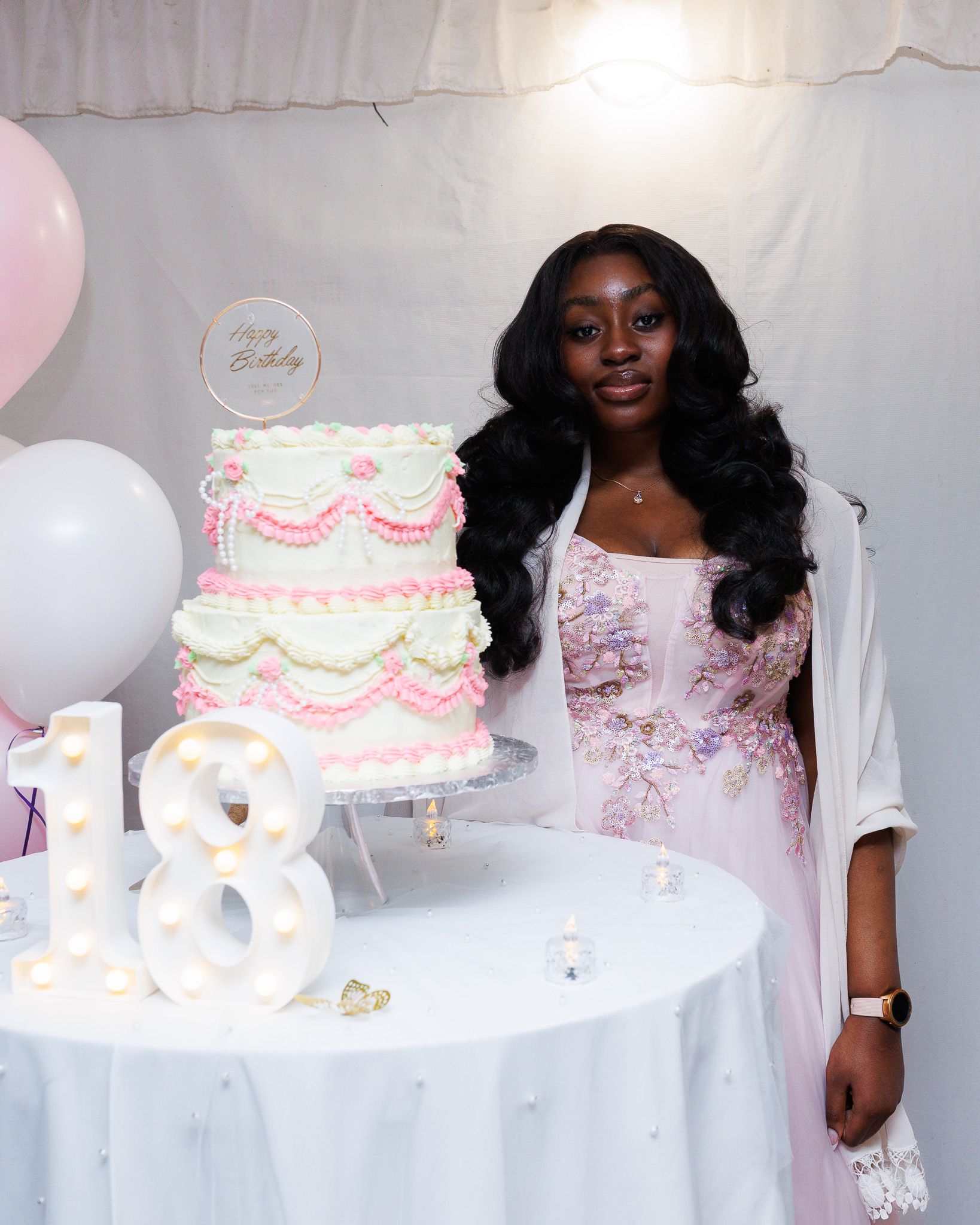 Pink and white tiered celebration cakes displayed on white tables with decorative details.