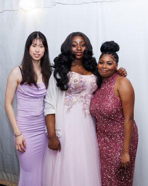 Three friends pose together in elegant evening gowns in shades of purple, pink and burgundy sequins.