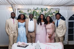 A wedding party poses together in formal attire with bridesmaids in pink dresses and groomsmen in tan suits.