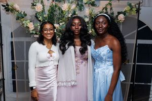 Wedding party members in pastel dresses gather under floral decorations at an elegant indoor venue.