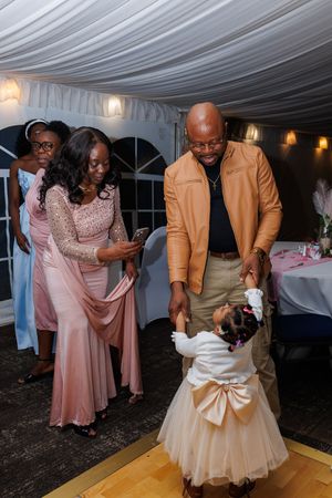 Guests dance and celebrate at an elegant wedding reception under a white draped tent with warm lighting.