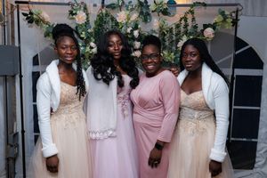 Wedding party members in pink and white dresses pose together for a formal group photo.