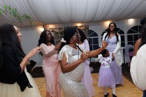 Wedding guests dance and celebrate together on a dance floor under a white tent at an evening reception.