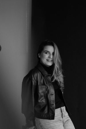 Casual portrait of woman in leather jacket and jeans against studio backdrop.