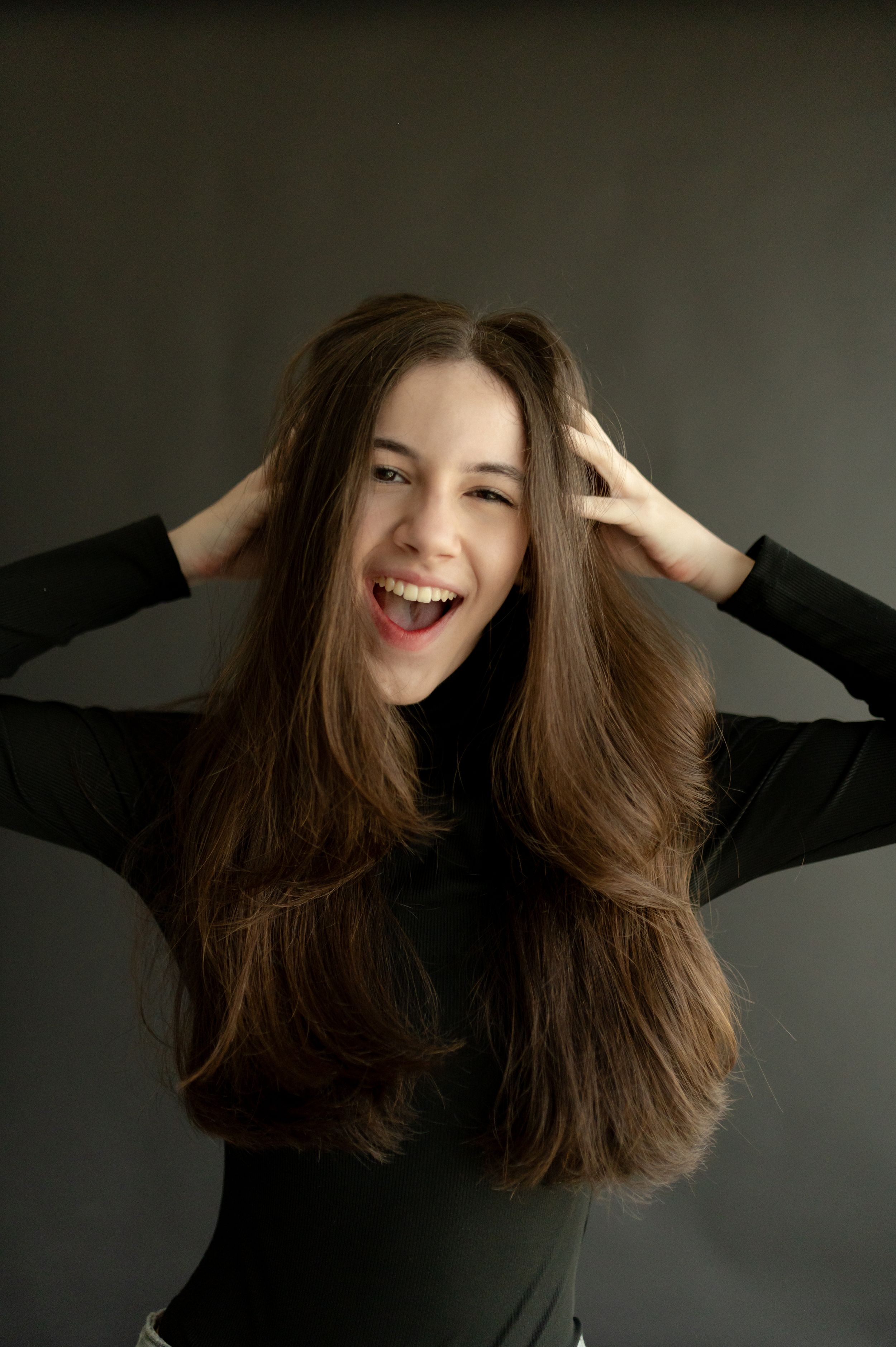 Energetic portrait showing playful hair toss moment against dark background.