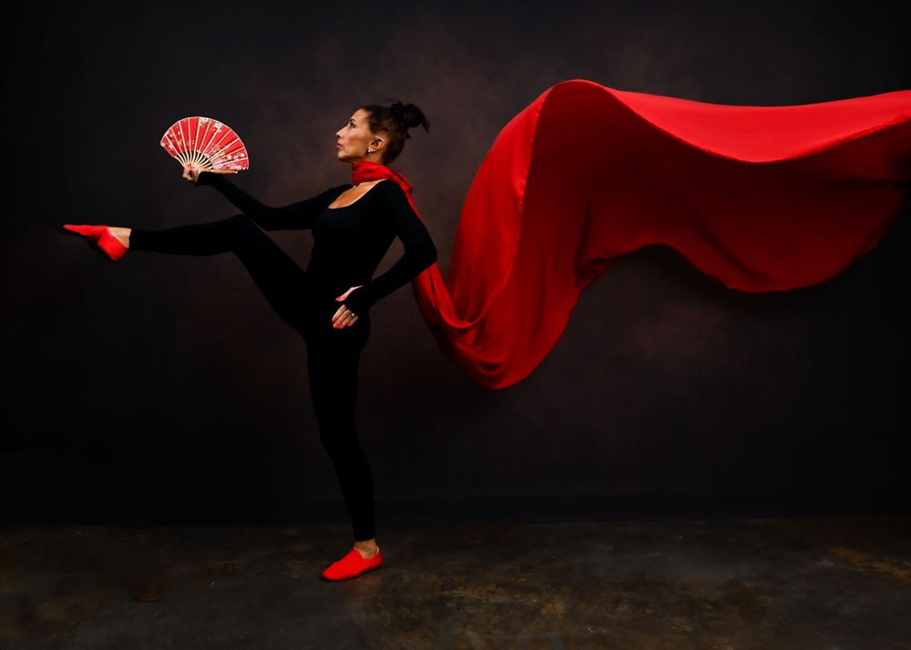 Dramatic dance pose with flowing red cape and fan against dark background.