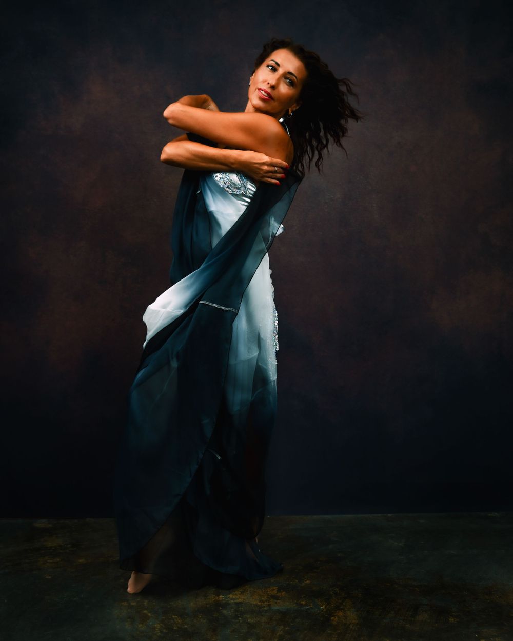 Contemporary dancer in flowing blue dress moves gracefully against dark background.