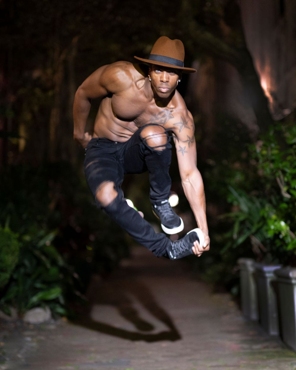 Athletic performer in hat executes dramatic jump in nighttime outdoor setting.