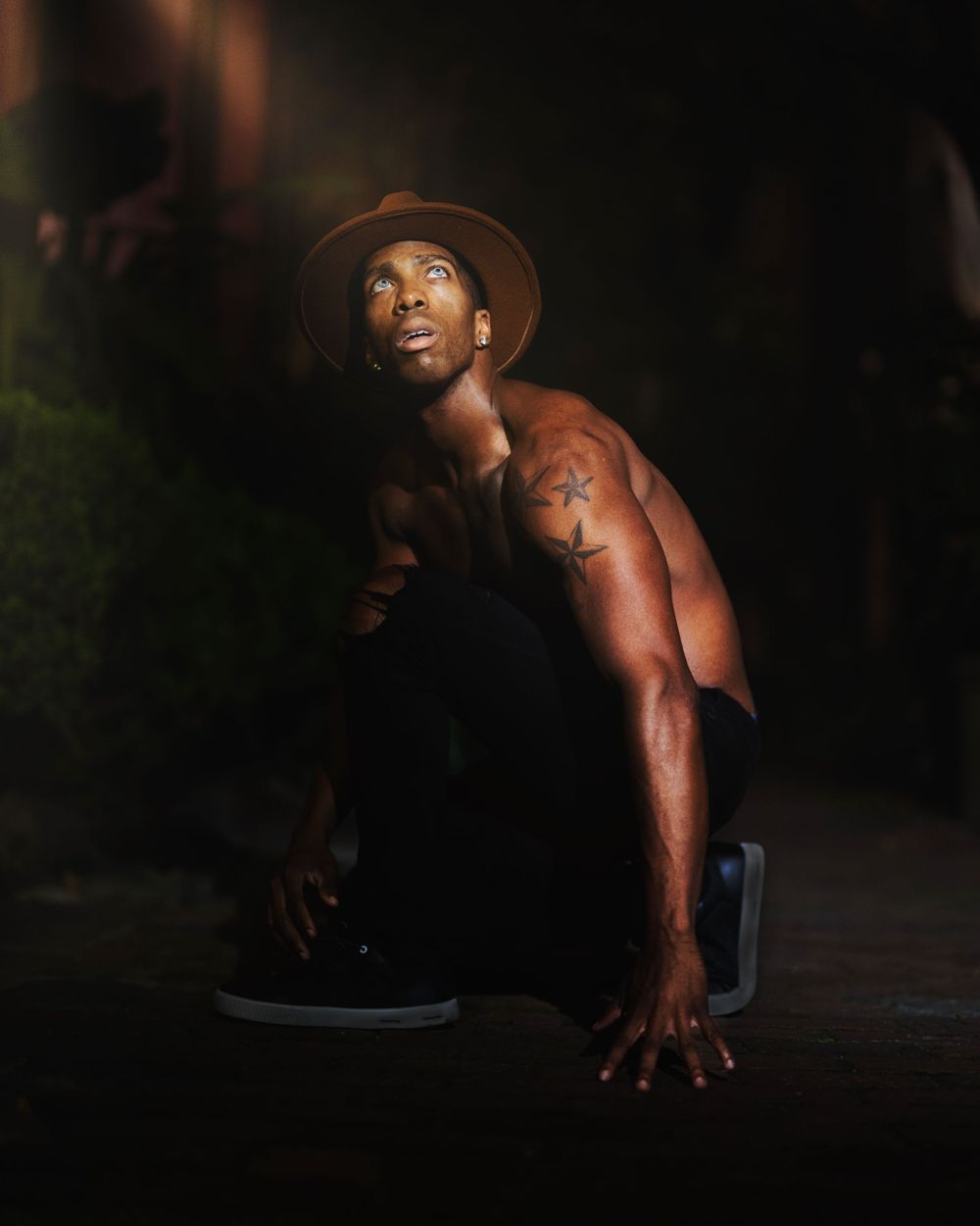 Athletic figure in hat crouches dramatically in low-key nighttime portrait.
