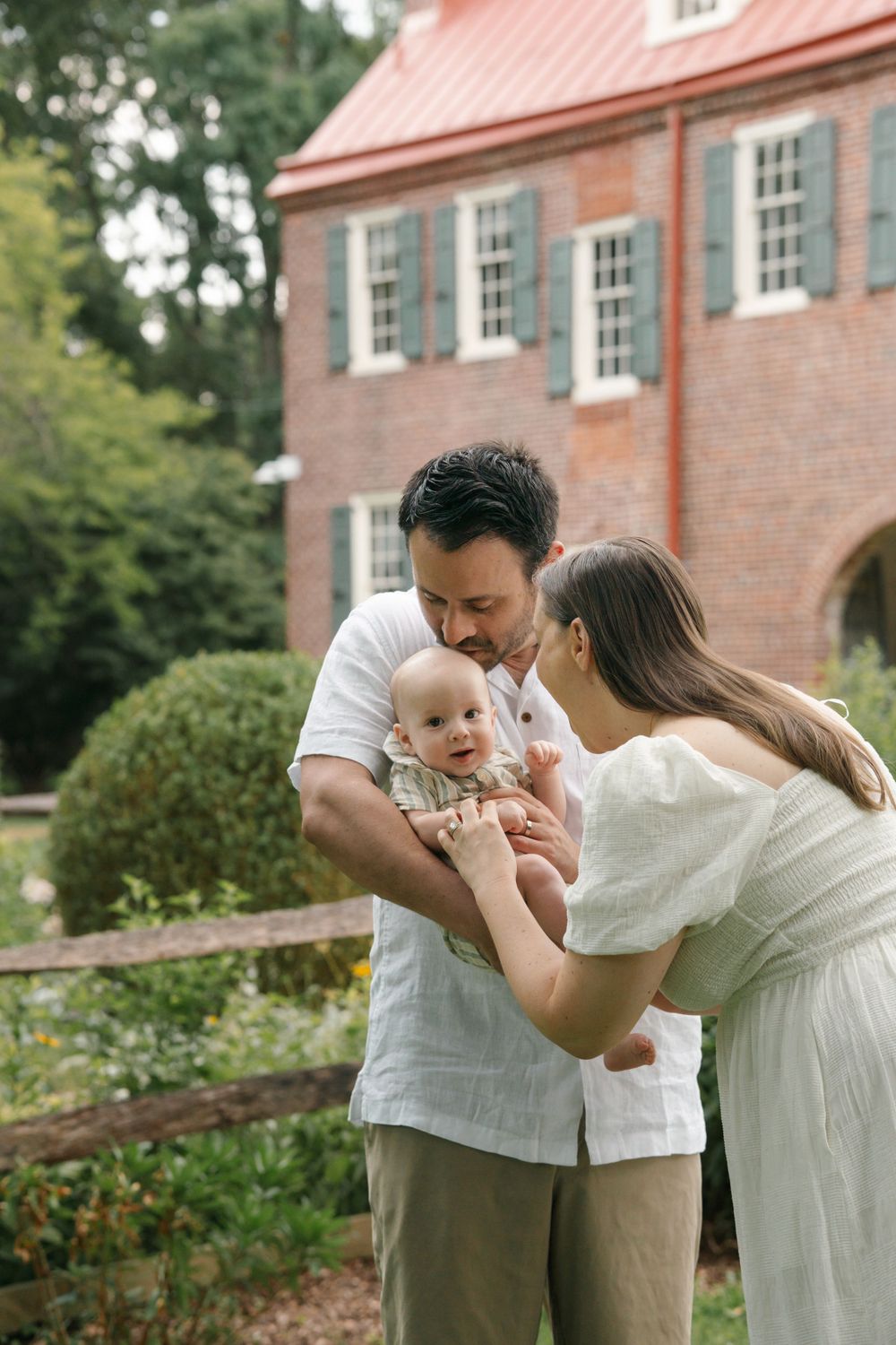 A loving family interacts with baby near the historic red brick building at Barclay Farmstead, in Cherry Hill, NJ.