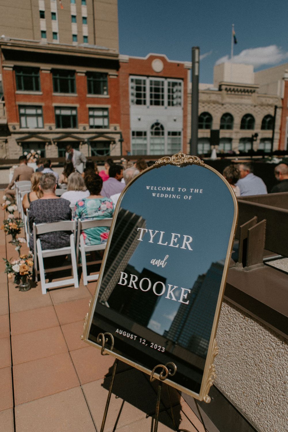 Wedding welcome sign for Tyler and Brooke displayed on an outdoor rooftop venue with city buildings in background.