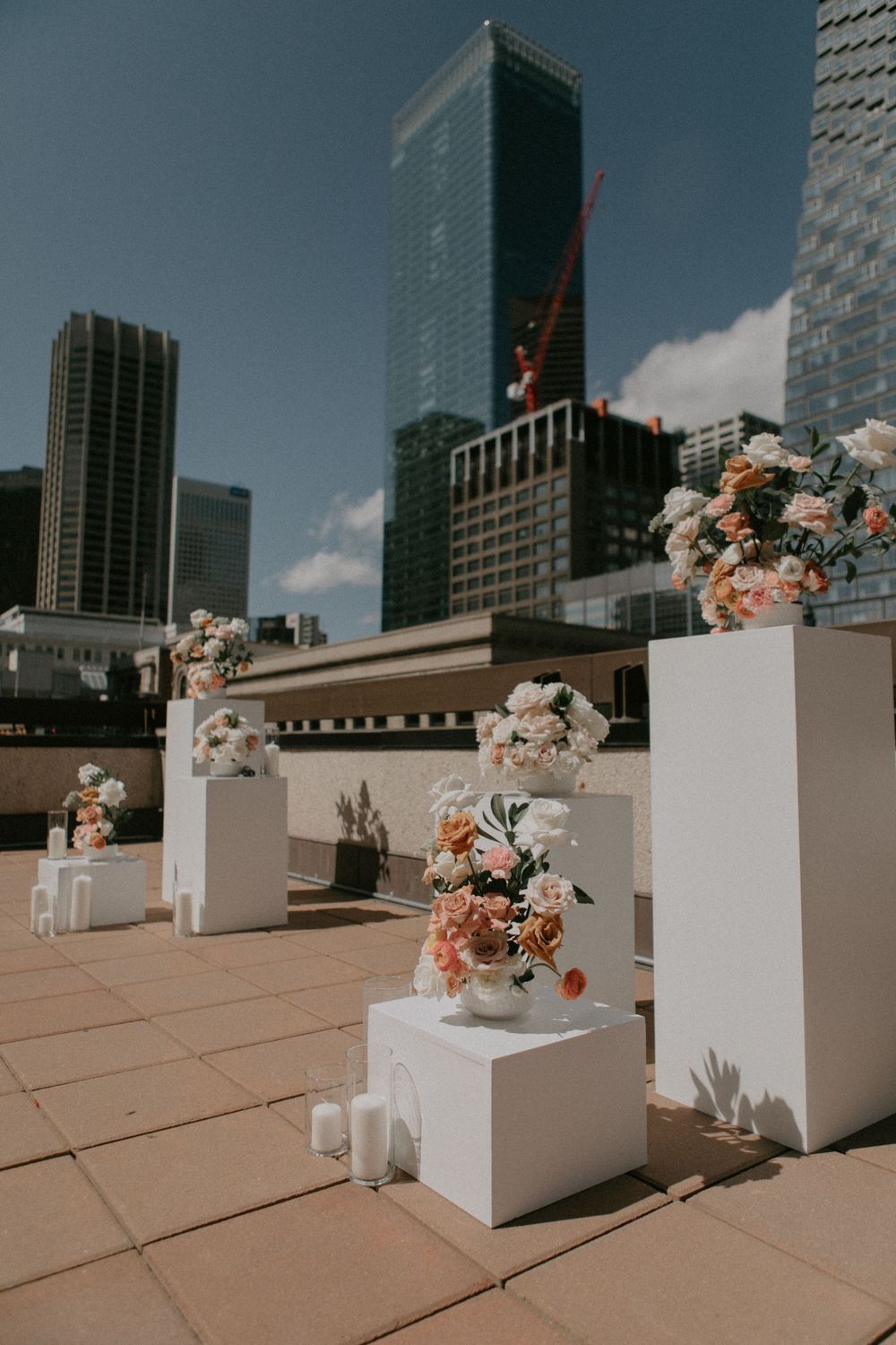 White floral arrangements on pedestals decorate a rooftop terrace with modern city skyscrapers in the background.