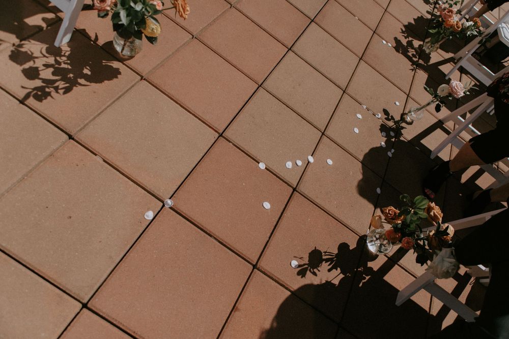 Geometric pattern of terracotta tiles with scattered flower petals and shadows on an urban rooftop.