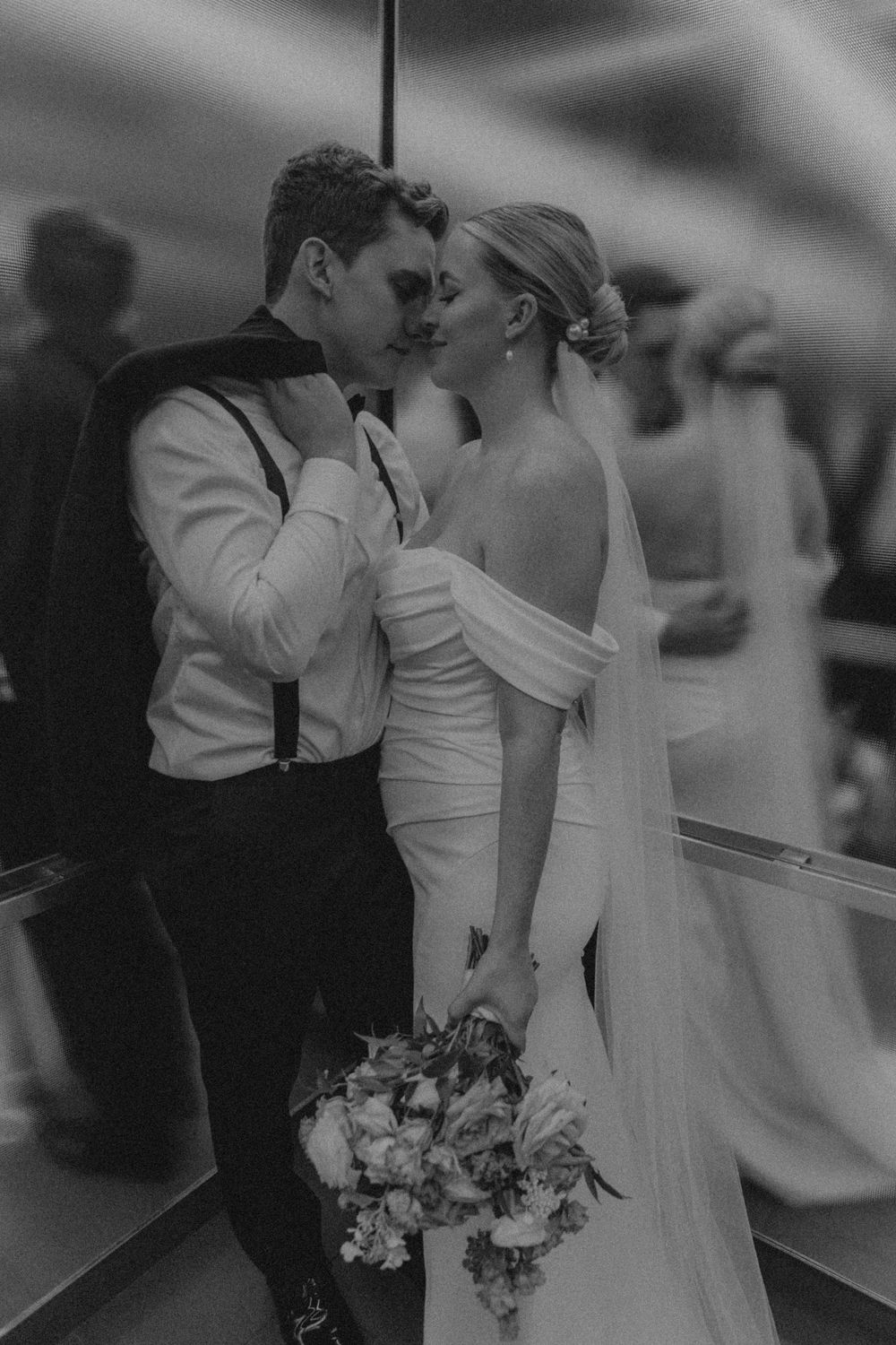 Romantic black and white portrait of newlyweds sharing an intimate moment with bouquet.