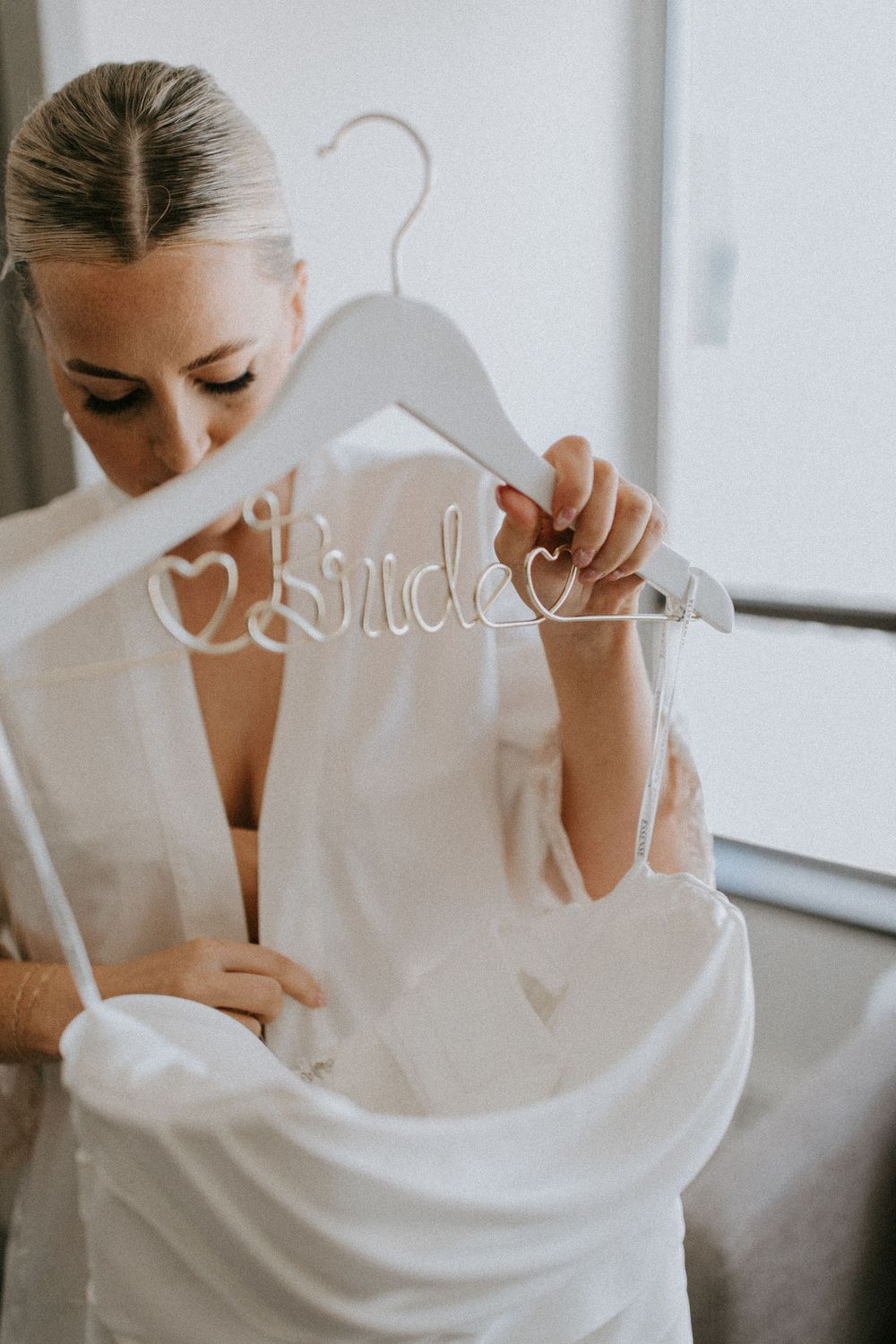 A white wooden hanger decorated with the word 'Bride' in elegant script is held up against a white robe.