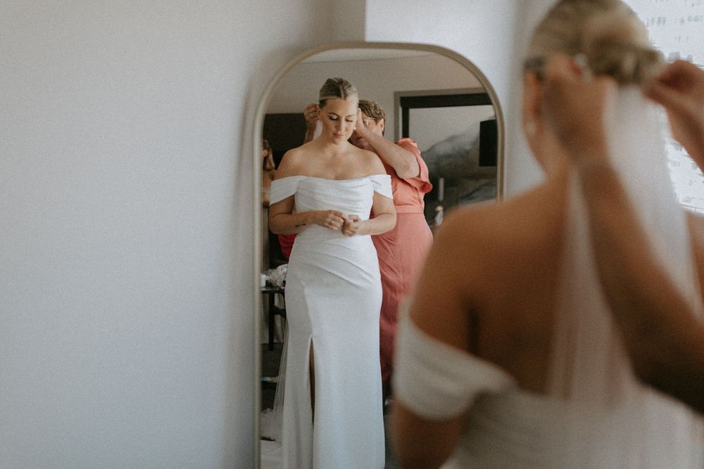 Bride trying on wedding dress while looking in a vintage mirror.