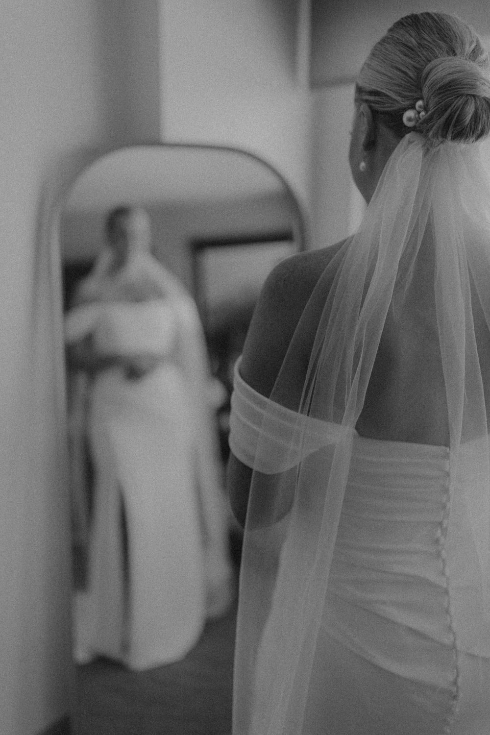 Black and white reflection of bride in wedding dress with flowing veil.