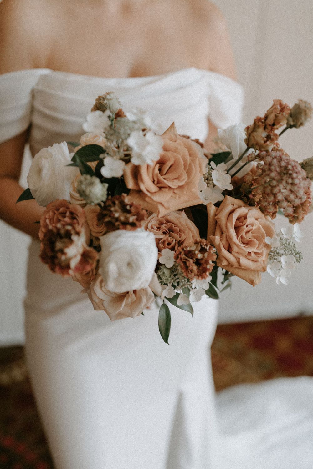 Elegant bridal bouquet with blush roses and white flowers against wedding dress.