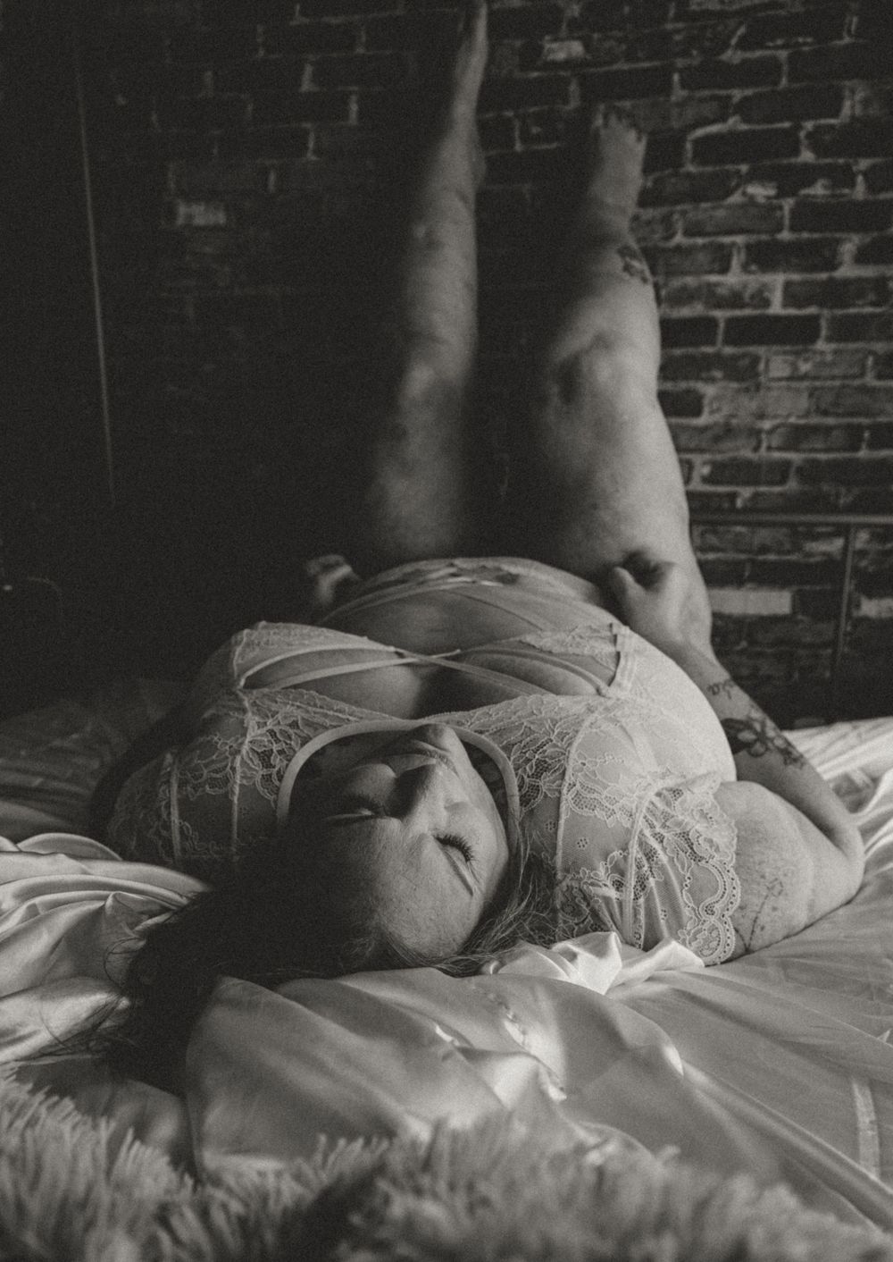 Artistic black and white boudoir photo with exposed brick wall backdrop.