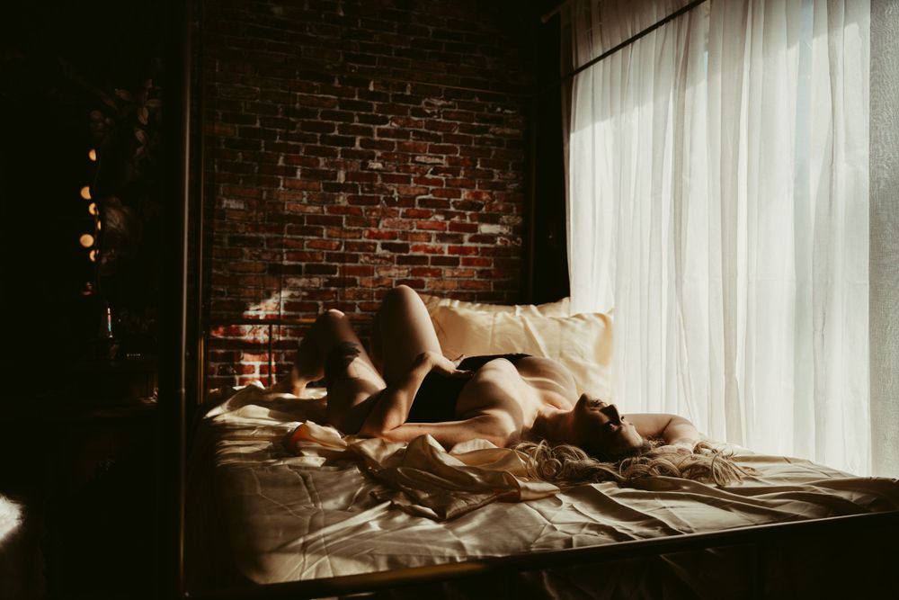 Silhouetted figure on bed with exposed brick wall and sheer curtains.