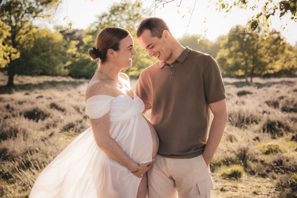 Een romantische zwangerschapsfotoshoot bij zonsondergang in een veld met warm gouden licht en een zachte, vloeiende witte jurk.