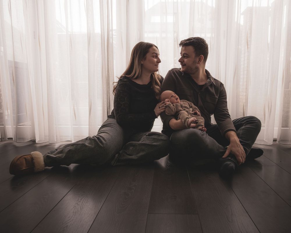 A romantic couple lounges together in silhouette against sheer curtains in a minimalist setting.