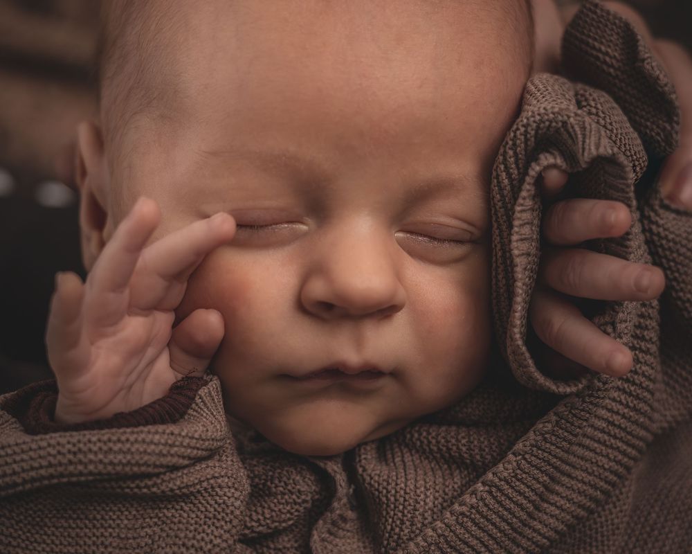 Een slapende baby, gewikkeld in een warme bruine gebreide deken, rust vredig in zacht en warm licht.