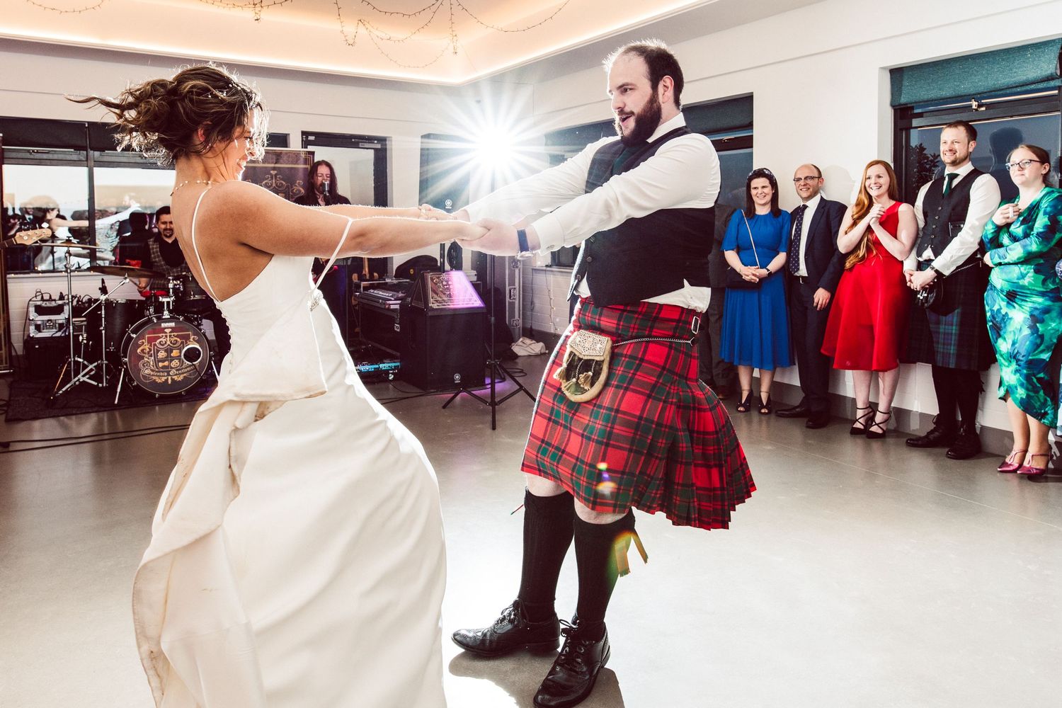 Couple performs a traditional Scottish dance in a bright reception hall with guests watching.