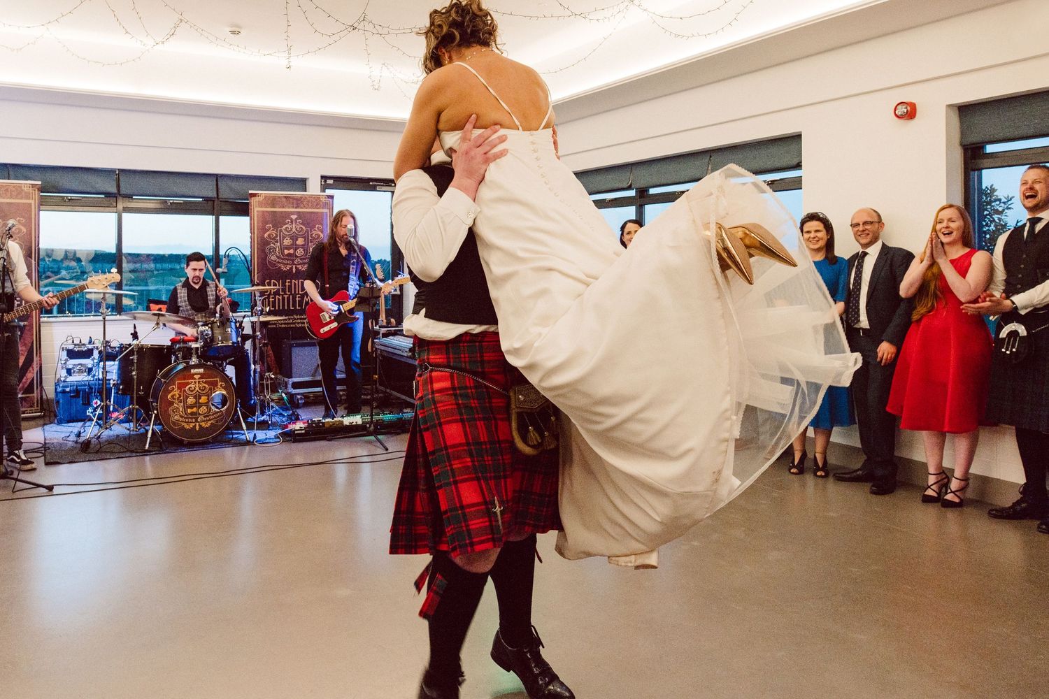 Wedding party dances in a spacious venue with guests watching from the sides.