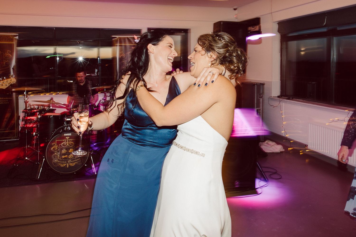 Two people share a romantic dance together on a dimly lit dance floor with pink lighting in the background.