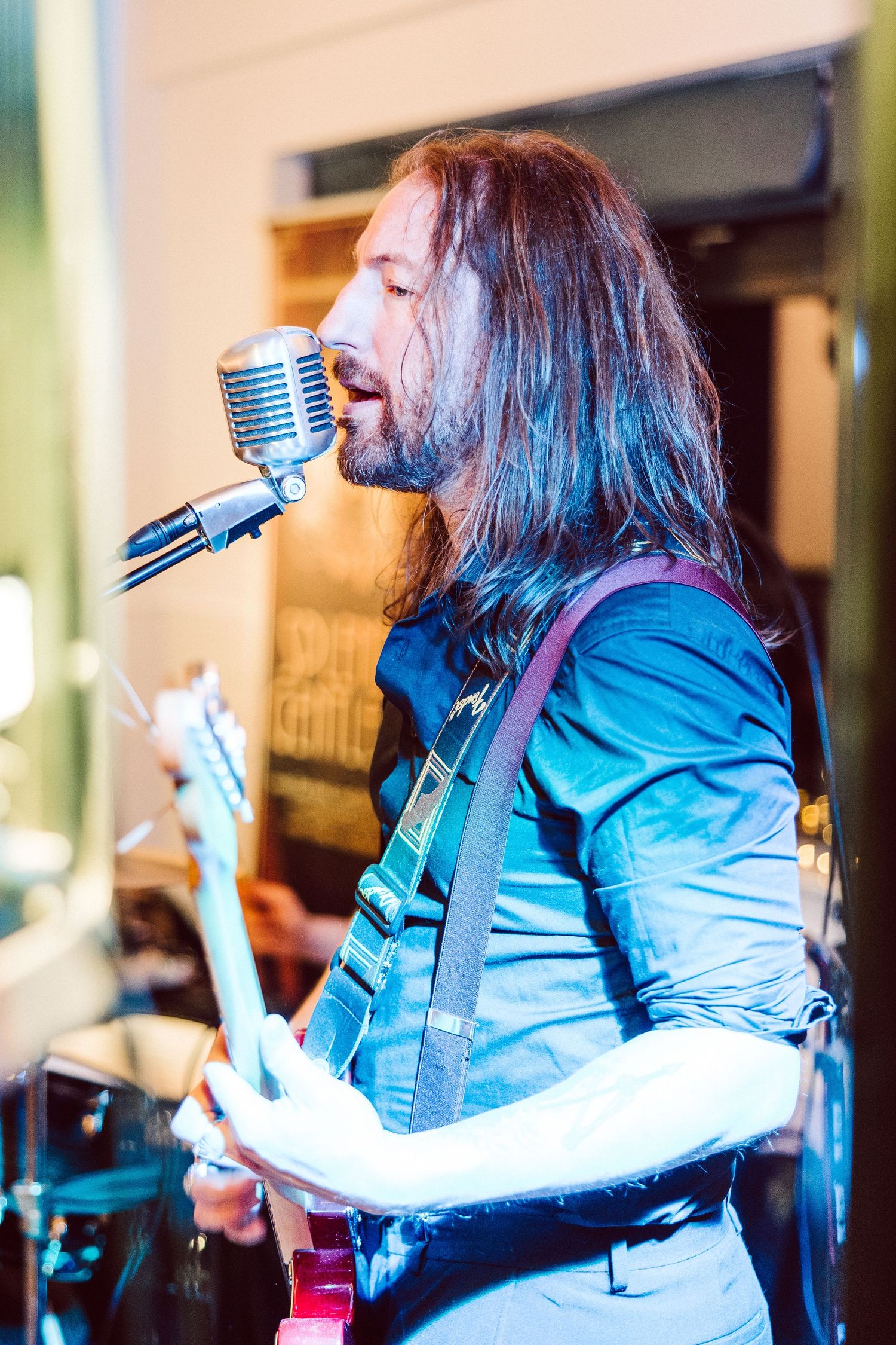 Musician in blue denim jacket performs with vintage microphone on stage.